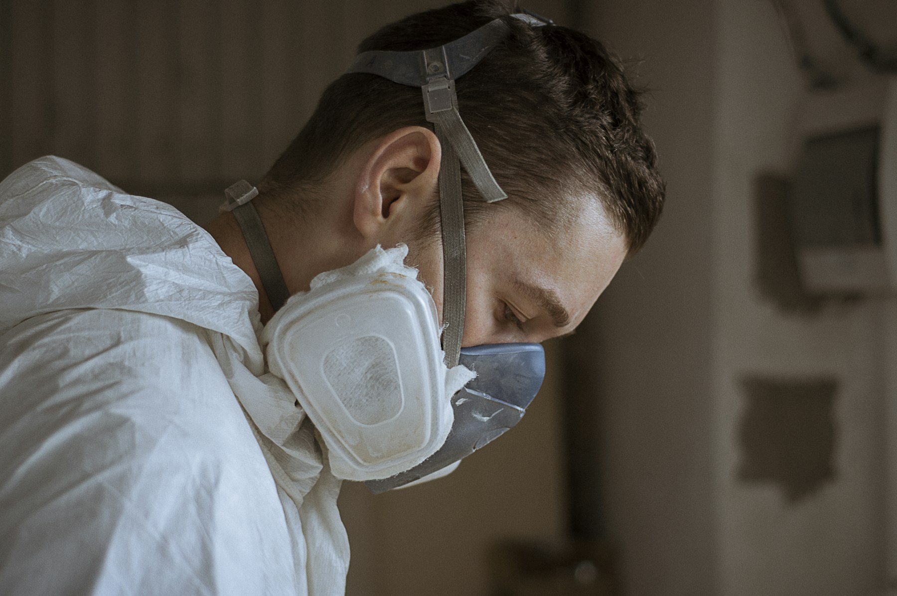 A worker in a white protective suit and half-face respirator