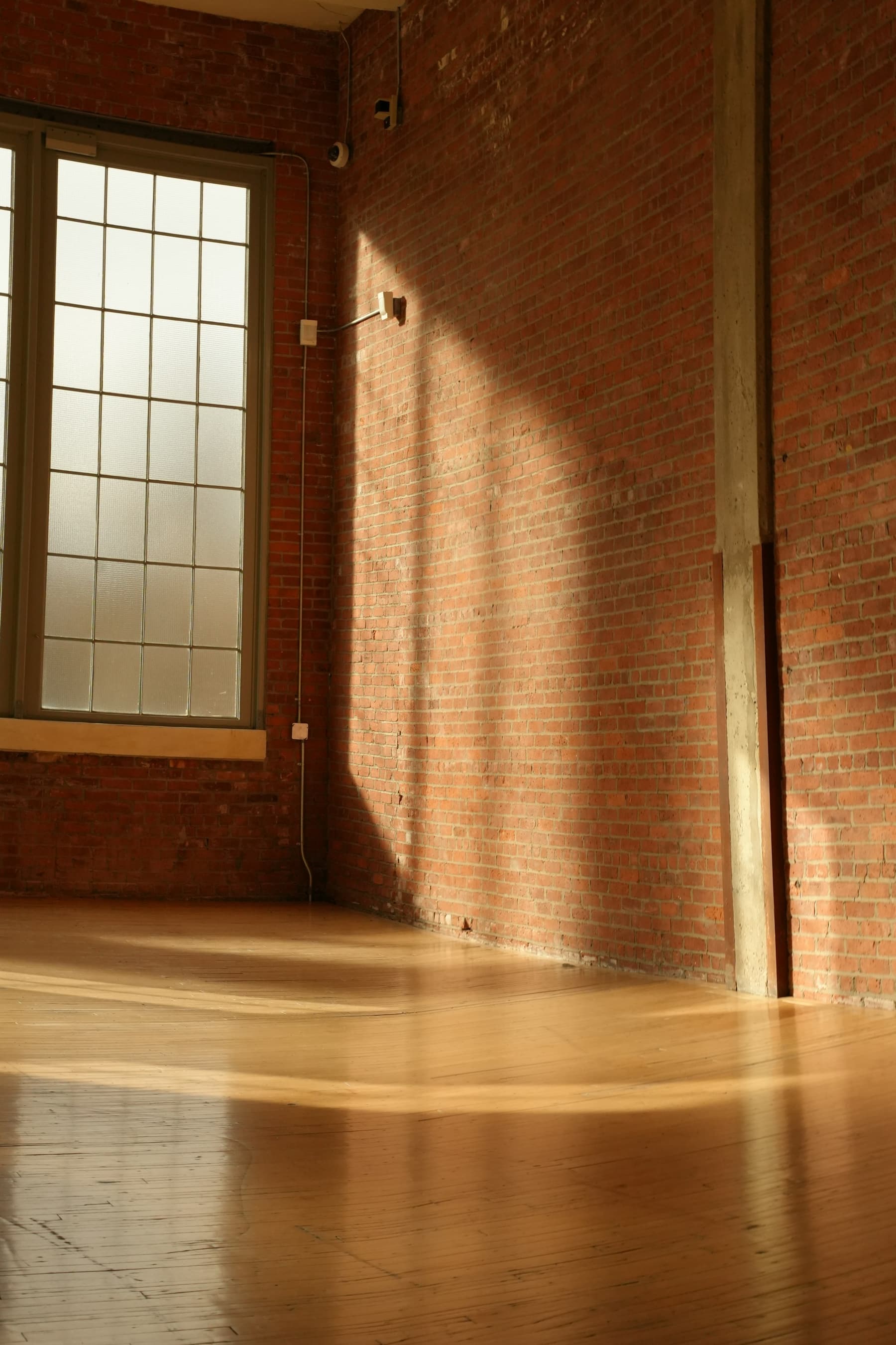 An empty loft with brick walls and warm sunlight streaming across a wooden floor