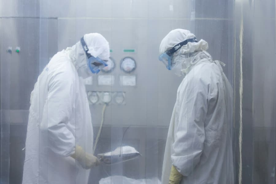 Two technicians in protective suits checking an instrument