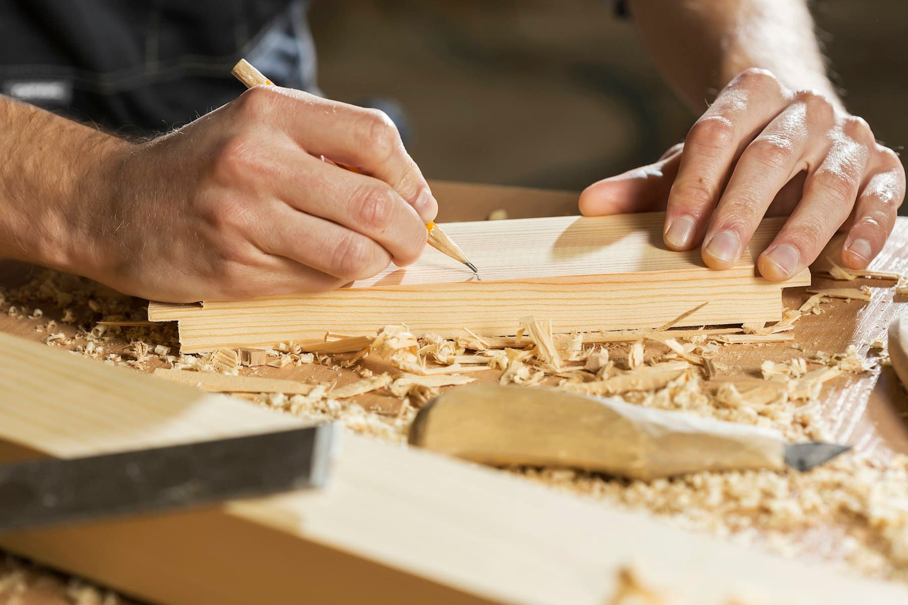 Hands marking a pine board with a pencil on a workbench covered in wood shavings